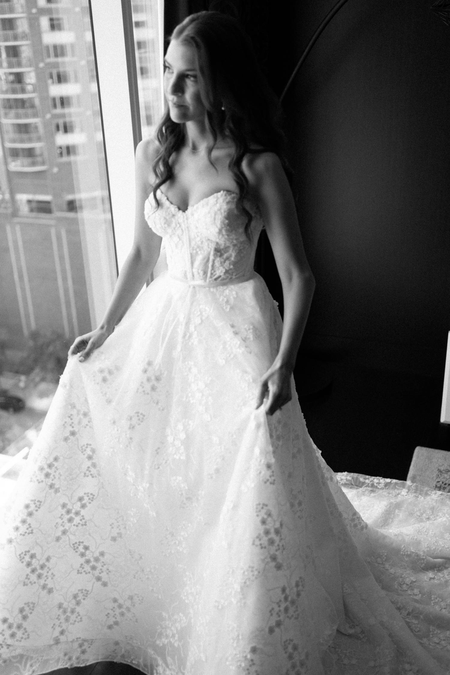 Bride looking out window and holding dress at Revel motor row Chicago wedding, photography by Allison Francois